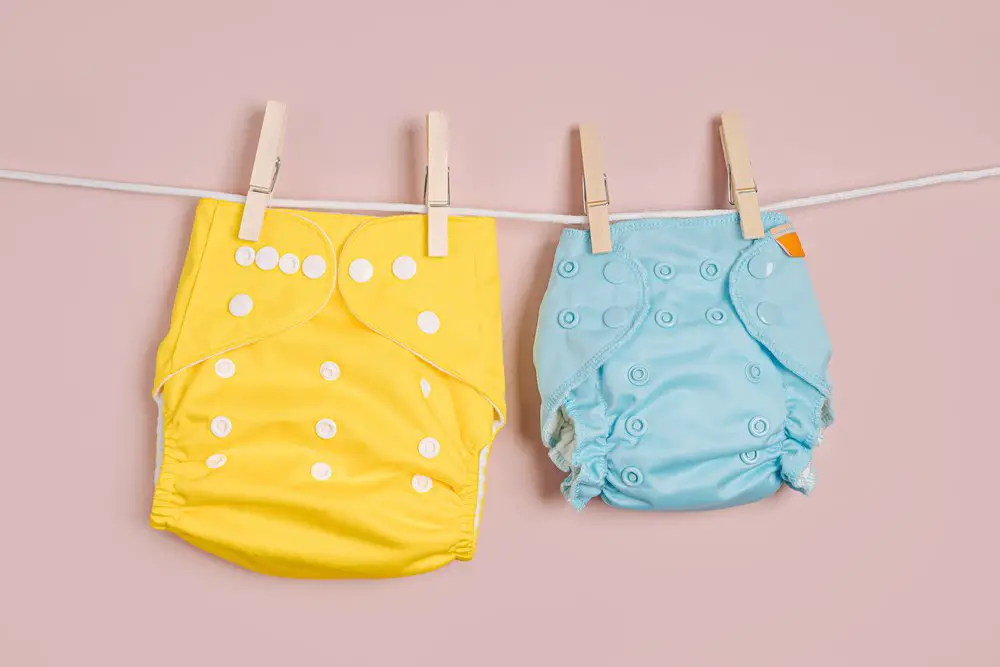 Reusable cloth baby diapers drying on a clothes line. Eco friendly cloth nappies on a pink background. Sustainable lifestyle. Zero waste concept.