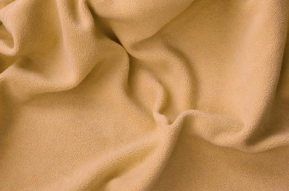 The blanket of furry orange fleece fabric. A background of light orange soft plush fleece material with a lot of relief folds