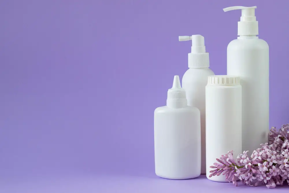 Jar with baby powder, bottle of talcum powder, liquid soap and shower gel isolated on a purple background with a branch of lilac.