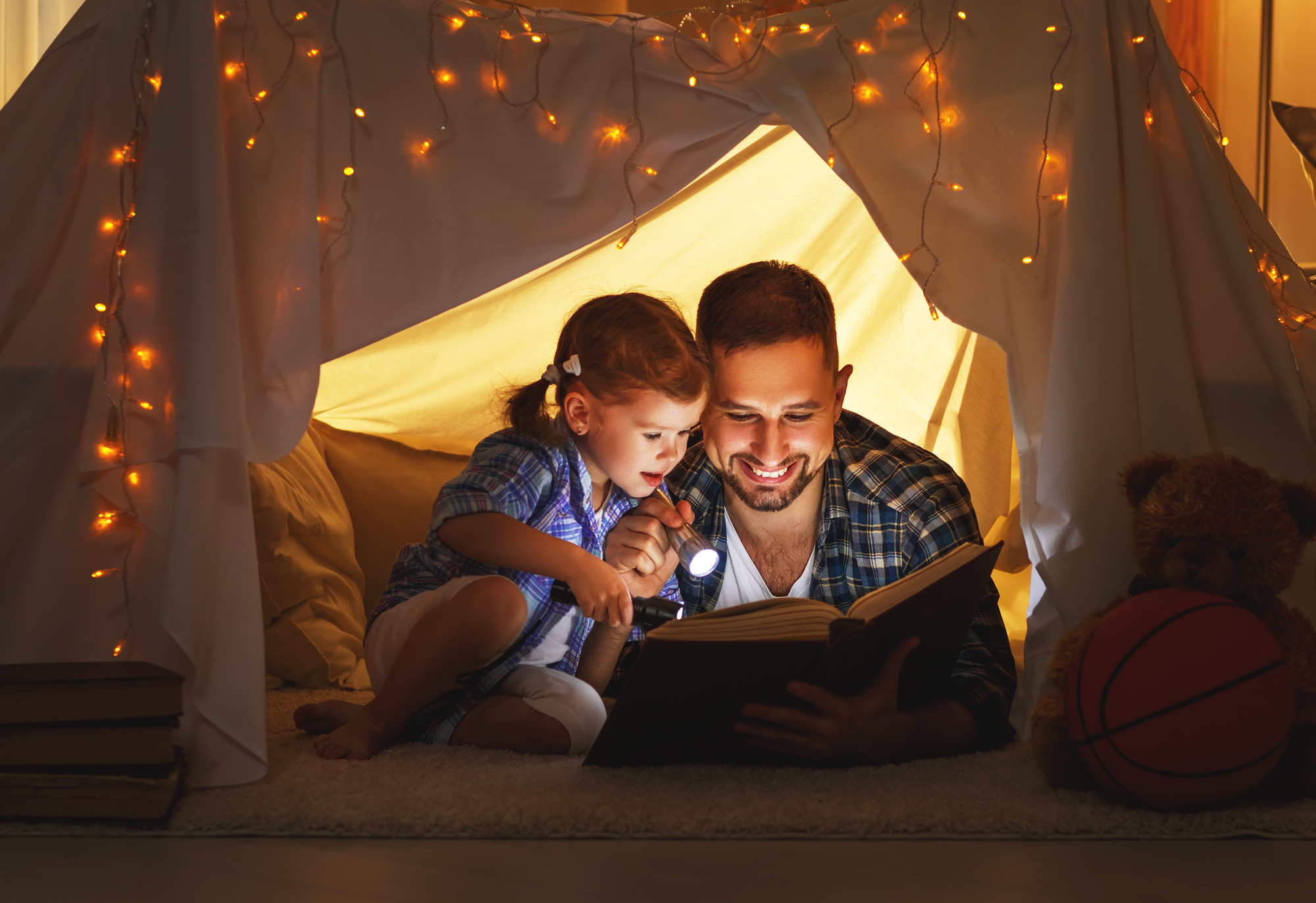 happy family father and child daughter reading a book in tent at home